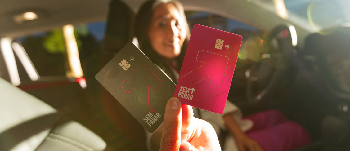 Mulher apresentando os cartões Sem Parar preto e rosa dentro de um carro.